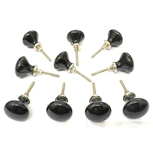 Peut inclure: Collection de dix boutons de meuble en céramique noire avec une finition brillante. Chaque bouton est équipé d'une vis métallique pour l'installation. Les boutons sont présentés dans différentes orientations.
