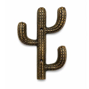 Puede incluir: Un gancho de pared de metal en tono bronce con forma de cactus saguaro. La superficie presenta un patrón texturizado y punteado en todo el cuerpo y los brazos. Dos orificios de montaje circulares están alineados verticalmente en el tallo.