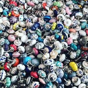 以下が含まれることがあります： 様々なパターンとデザインのカラフルなセラミック製のキャビネットノブの大きなコレクション。ノブはすべて形とサイズが異なり、ランダムなパターンで配置されています。