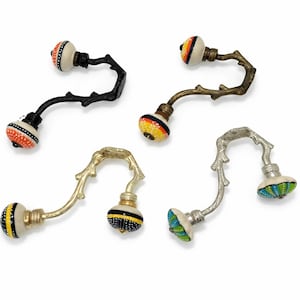 Puede incluir: Cinco tiradores decorativos para armarios con diseño de rama. Los tiradores tienen esferas de cerámica estampadas y coloridas en naranja, amarillo, negro y azul. Los brazos metálicos son en tonos negro, dorado y plateado.