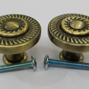 Pu&ograve; includere: Due pomelli per armadi in oro antico con un design a raggiera e un bordo decorativo. I pomelli sono forniti con due viti.