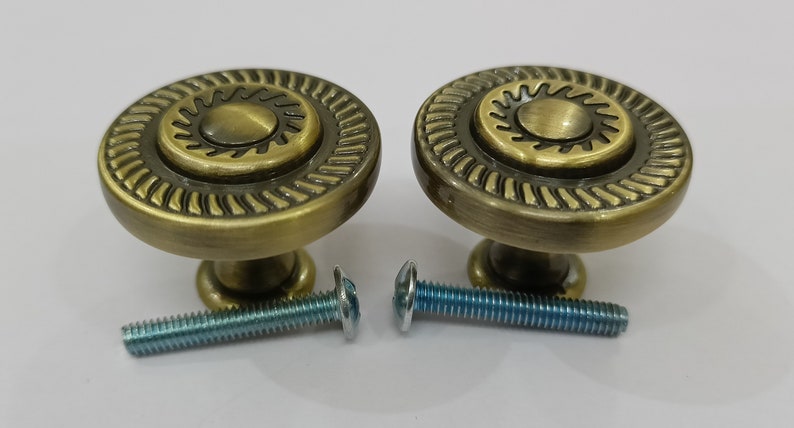 Pu&ograve; includere: Due pomelli per armadi in oro antico con un design a raggiera e un bordo decorativo. I pomelli sono forniti con due viti.