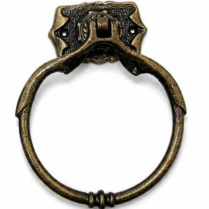 Puede incluir: Un tirador de anillo de metal en tono lat&oacute;n antiguo con un acabado texturizado y desgastado. El anillo circular est&aacute; unido a una placa de montaje rectangular decorativa con detalles en relieve y dos orificios visibles para tornillos.