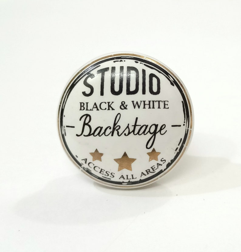 May include: White ceramic knob with a black and gold design. The knob features the text "Studio Black & White - Backstage - Access All Areas" and three gold stars.