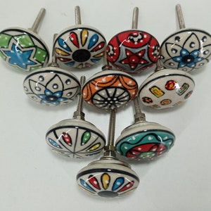 Op de afbeelding: Een verzameling van tien keramische kastknoppen met diverse kleurrijke patronen. Elke knop heeft een zilveren metalen schroef. De ontwerpen omvatten bloemen, geometrische en abstracte vormen in blauw, groen, rood, oranje en geel.