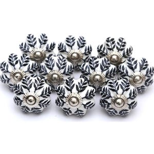 Puede incluir: Un conjunto de tiradores de armario con forma floral. Cada tirador presenta una base blanca con un diseño de hojas negras y un centro de metal plateado. Adecuado para muebles y decoración del hogar.