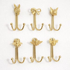 Puede incluir: Seis ganchos de pared de metal dorado. Cada gancho tiene una parte superior decorativa: un conejito, un lazo, un zorro, una abeja, un murciélago y otra abeja. Cada gancho tiene dos ganchos curvos para colgar objetos.