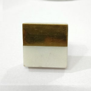 K&ouml;nnte beinhalten: Eine rechteckige dekorative Box mit einem wei&szlig;en Marmorsockel und einer goldfarbenen Metalloberseite. Die Box hat eine einfache, geometrische Form, und die kontrastierenden Materialien erzeugen eine moderne &Auml;sthetik. Die Box wird wahrscheinlich zur Aufbewahrung oder Pr&auml;sentation verwendet.