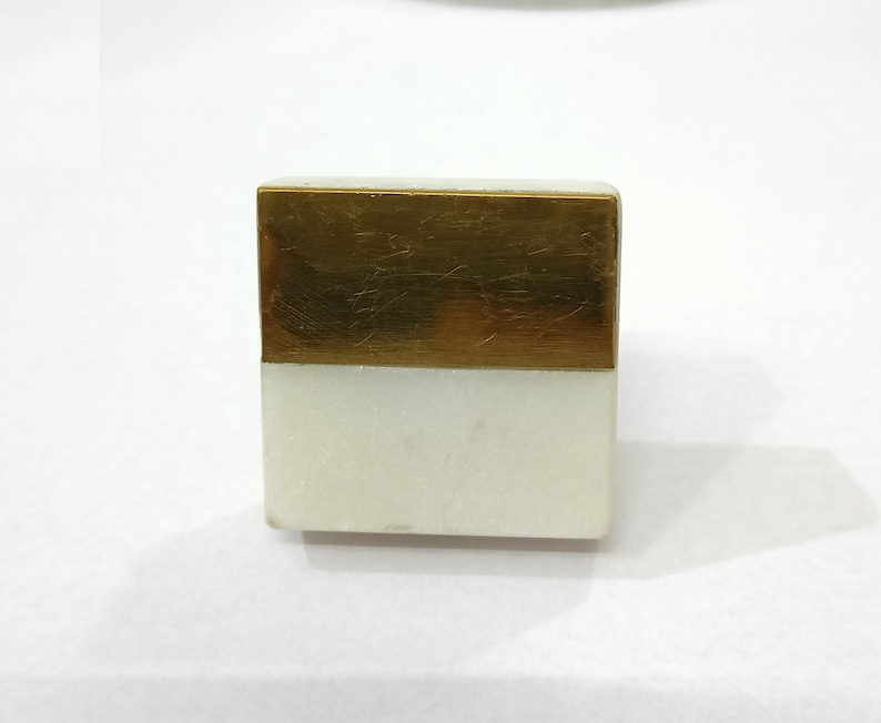 K&ouml;nnte beinhalten: Eine rechteckige dekorative Box mit einem wei&szlig;en Marmorsockel und einer goldfarbenen Metalloberseite. Die Box hat eine einfache, geometrische Form, und die kontrastierenden Materialien erzeugen eine moderne &Auml;sthetik. Die Box wird wahrscheinlich zur Aufbewahrung oder Pr&auml;sentation verwendet.