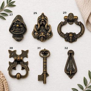May include: Six antique brass-toned metal furniture pulls and door knockers labeled 27 through 32. Item 27 is a hooded figure, 28 is a decorative mask, 29 is a ring pull with a face, 30 is a gothic-style pull, 31 is a key, and 32 is a teardrop pull.