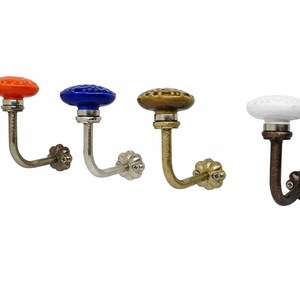 May include: Four decorative wall hooks with colorful ceramic knobs. The knobs are orange, blue, gold, and white. The hooks have a curved design and are made of metal. These hooks are ideal for hanging coats, hats, or other items.