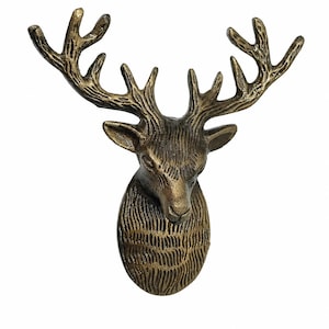 Puede incluir: Una escultura de pared con forma de cabeza de ciervo y acabado en tono bronce oscuro. La pieza presenta patrones de pelaje texturizados y detallados en el cuello y la cara, con astas ramificadas prominentes que se extienden desde la cabeza.