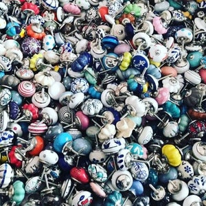 Op de afbeelding: Een grote verzameling kleurrijke keramische kastknoppen met verschillende patronen en ontwerpen. De knoppen zijn allemaal in verschillende vormen en maten en zijn in een willekeurig patroon gerangschikt.