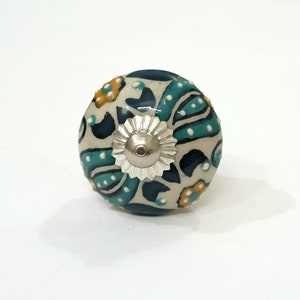Op de afbeelding: Een witte keramische knop met een blauw en groen bloemenpatroon en een zilveren metalen midden.