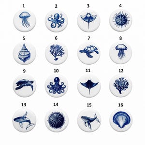 Peut inclure: Une collection de seize boutons ronds en céramique blanche avec des motifs de créatures marines bleues. Les motifs comprennent une méduse, une pieuvre, une raie, un oursin, un coquillage, du corail, une tortue de mer et une baleine.