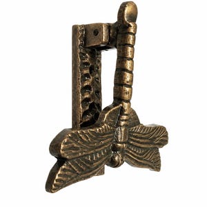 Puede incluir: Un llamador de puerta de metal en tono bronce con forma de lib&eacute;lula, alas texturizadas y cuerpo segmentado. La lib&eacute;lula est&aacute; unida a una placa de montaje vertical rectangular que presenta un acabado de superficie martillado y r&uacute;stico.