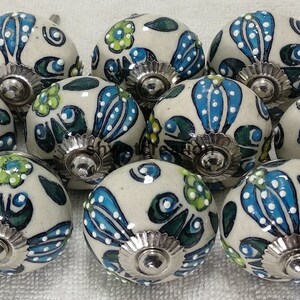 May include: Ten ceramic cabinet knobs with a white base and blue, green, and yellow floral designs. Each knob has a silver metal base.