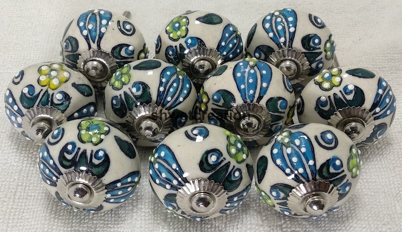 May include: Ten ceramic cabinet knobs with a white base and blue, green, and yellow floral designs. Each knob has a silver metal base.