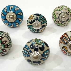 Op de afbeelding: Zes keramische knoppen met ingewikkelde bloemmotieven in tinten blauw, groen, rood en geel. Elke knop heeft een zilveren metalen centrum.