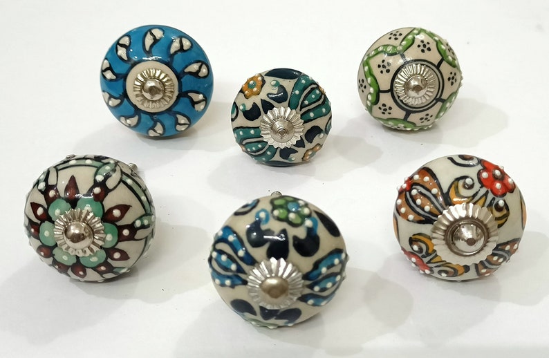 Op de afbeelding: Zes keramische knoppen met ingewikkelde bloemmotieven in tinten blauw, groen, rood en geel. Elke knop heeft een zilveren metalen centrum.