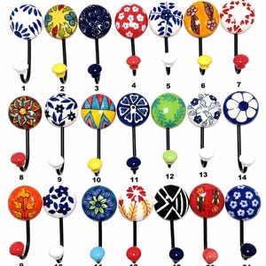 May include: A collection of decorative ceramic wall hooks with various colorful floral and geometric designs. Each hook has a black metal stem and a coordinating knob at the base. The hooks are numbered 1 through 21.