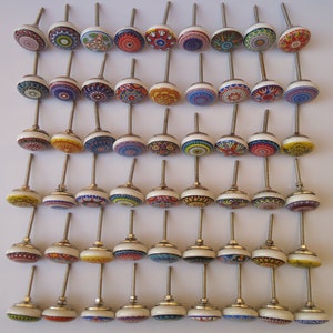 Puede incluir: Una colecci&oacute;n de 48 pomos de armario de cer&aacute;mica coloridos con intrincados patrones. Cada pomo presenta un dise&ntilde;o &uacute;nico con una variedad de colores, incluyendo azul, rojo, verde, amarillo y blanco. Los pomos est&aacute;n unidos a tornillos de metal plateado.