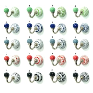 Op de afbeelding: Een verzameling decoratieve keramische wandhaken met metalen beslag. Elke haak heeft een ronde, kleurrijke knop en een keramische basis met patroon. Kleuren zijn onder meer groen, blauw, grijs, rood en zwart. De haken zijn in een raster gerangschikt.