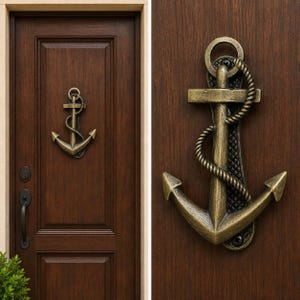 May include: A brass-colored metal door knocker shaped like a nautical anchor with a rope detail wrapped around the central shaft. The anchor is mounted on a dark brown wooden door with a vertical panel design and a black metal handle below it.