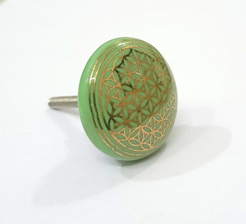 May include: Green ceramic cabinet knob with a gold flower of life design.