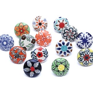 Puede incluir: Una colección de pomos decorativos de cerámica con diversos colores y diseños florales. Los pomos redondos están pintados a mano con intrincados patrones en tonos azules, naranjas, verdes y blancos. Ideales para añadir un toque único a los muebles, aprox. 3-4 cm de diámetro.