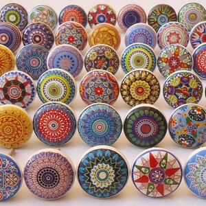 Pu&ograve; includere: Assortimento di pomelli in ceramica colorati con intricati disegni di mandala. I pomelli sono rotondi e hanno una base bianca con vari colori e motivi.