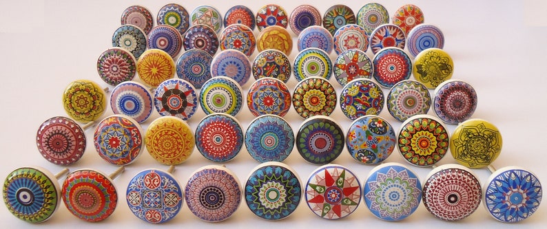 Pu&ograve; includere: Assortimento di pomelli in ceramica colorati con intricati disegni di mandala. I pomelli sono rotondi e hanno una base bianca con vari colori e motivi.