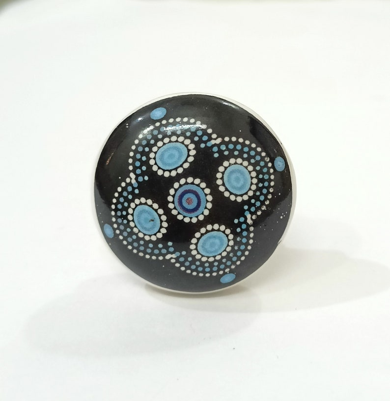 May include: A black ceramic knob with a blue and white dot pattern. The pattern is a series of concentric circles with a blue centre and white dots around the edge.