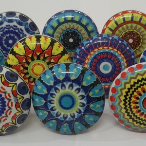 Może przedstawiać: Zestaw dziesięciu kolorowych ceramicznych gałek do szafek z wzorami mandali. Każda gałka ma inny wz&oacute;r w odcieniach niebieskiego, czerwonego, ż&oacute;łtego, zielonego i białego.