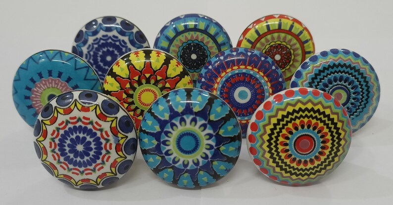 Może przedstawiać: Zestaw dziesięciu kolorowych ceramicznych gałek do szafek z wzorami mandali. Każda gałka ma inny wz&oacute;r w odcieniach niebieskiego, czerwonego, ż&oacute;łtego, zielonego i białego.