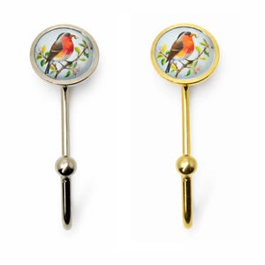 May include: Two decorative wall hooks. One hook has a silver finish, and the other has a gold finish. Each hook features a round, glass-covered image of a bird perched on a flowering branch. The bird has red, brown, and orange feathers.