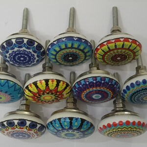 Może przedstawiać: Dziesięć kolorowych ceramicznych gałek do szafek z misternymi wzorami mandali. Każda gałka ma inną kombinację kolor&oacute;w i wz&oacute;r, w tym niebieski, zielony, czerwony, ż&oacute;łty i biały.