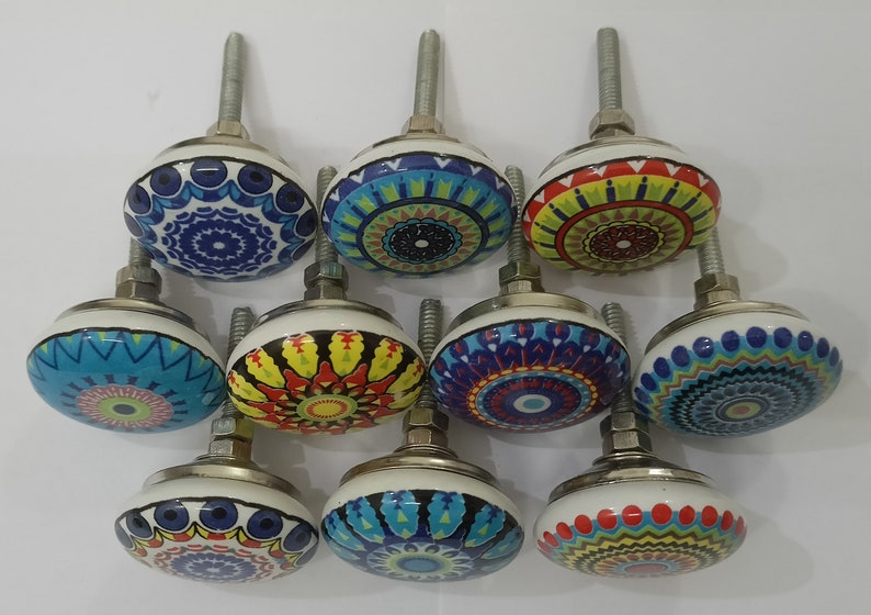 Może przedstawiać: Dziesięć kolorowych ceramicznych gałek do szafek z misternymi wzorami mandali. Każda gałka ma inną kombinację kolor&oacute;w i wz&oacute;r, w tym niebieski, zielony, czerwony, ż&oacute;łty i biały.