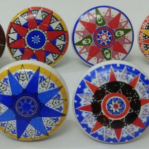 May include: Eight ceramic knobs featuring a starburst design in a variety of colours, including red, blue, green, yellow, and white. The knobs have a raised starburst design in the centre and a decorative border around the edge.