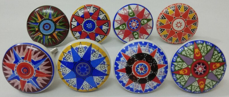 May include: Eight ceramic knobs featuring a starburst design in a variety of colours, including red, blue, green, yellow, and white. The knobs have a raised starburst design in the centre and a decorative border around the edge.