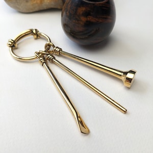 May include: A gold-toned pipe tool set with three tools attached to a ring. The tools include a tamper, a reamer, and a pick. The tools are made of metal and have a polished finish.