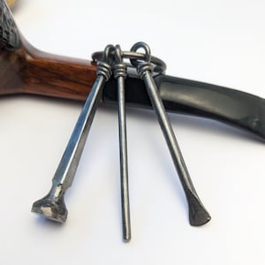 May include: Three metal pipe tools with a ring attached to a wooden pipe. The tools are made of dark metal and have a pointed tip.