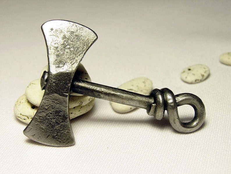 May include: A silver-colored metal axe pendant with a knotted handle. The axe head is double-sided and has a hammered finish.