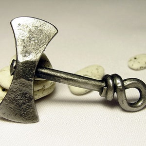 May include: A silver double-headed axe with a knotted handle. The axe is resting on a pile of white stones.