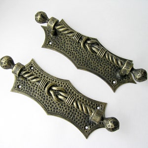 以下が含まれることがあります： ロープのデザインとハンマーで打たれた金属の仕上げを施した、アンティーク調のドアノブ2個。ノブは真鍮製で、装飾的な結び目のデザインが施されています。