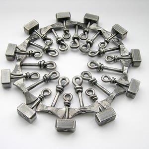 May include: A circle of 18 silver metal hammer charms, each with a different design. The charms are connected by a ring.
