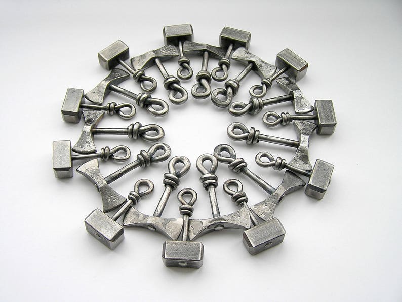 May include: A circle of 18 silver metal hammer charms, each with a different design. The charms are connected by a ring.