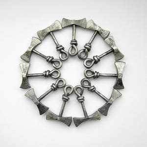 May include: A circle of 12 silver-colored metal axe-shaped bottle openers arranged in a circle. The axe heads are facing outward and the handles are connected in the center.