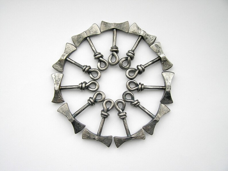 May include: A circle of 12 silver-colored metal axe-shaped bottle openers arranged in a circle. The axe heads are facing outward and the handles are connected in the center.