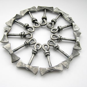 May include: A set of twelve silver metal axe-shaped bottle openers arranged in a circle. The axe heads are connected by a loop at the top.